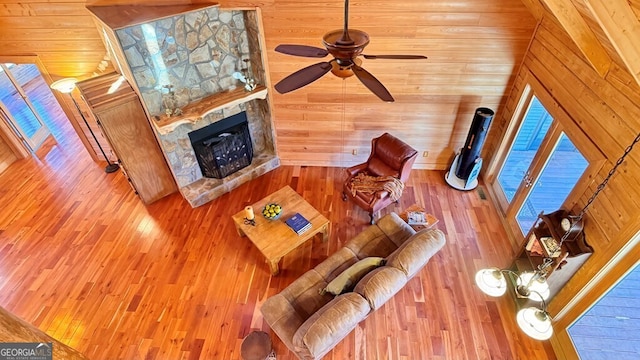 living area featuring a ceiling fan, a fireplace, wood walls, and wood finished floors