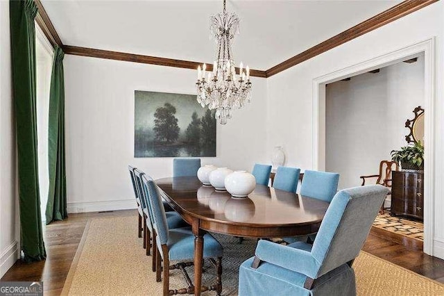 dining space with dark wood-type flooring, ornamental molding, and an inviting chandelier