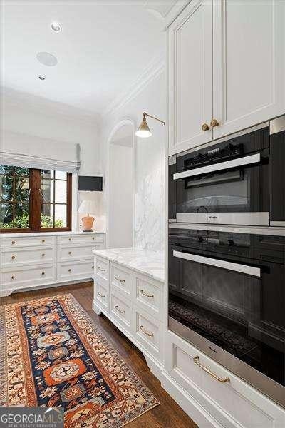 kitchen featuring dark wood-type flooring, double oven, white cabinets, and light stone counters