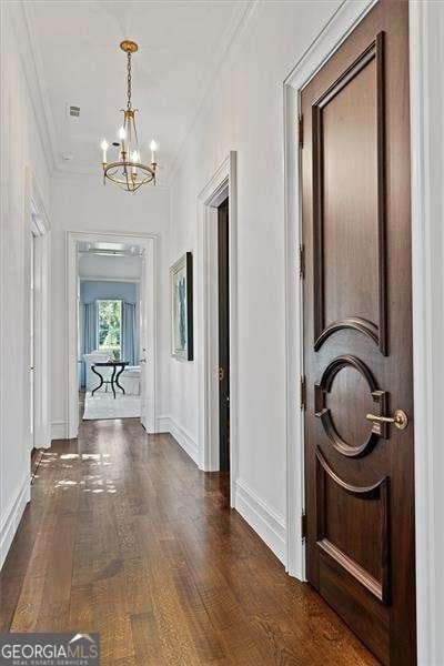 hallway with dark hardwood / wood-style floors, ornamental molding, and a notable chandelier