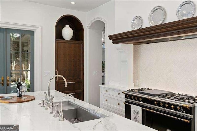 kitchen featuring extractor fan, tasteful backsplash, range with two ovens, light stone countertops, and sink