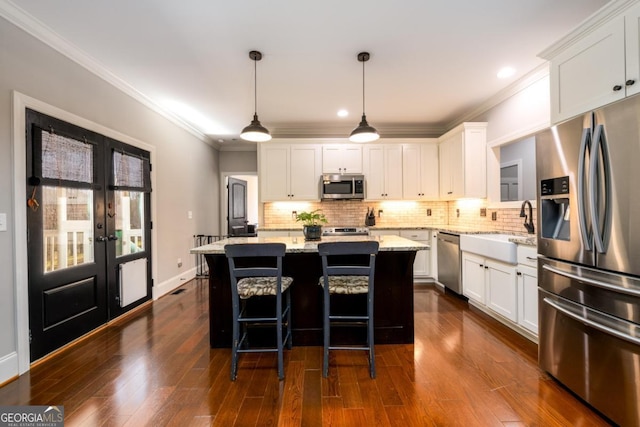 kitchen with sink, white cabinetry, decorative light fixtures, appliances with stainless steel finishes, and a kitchen island