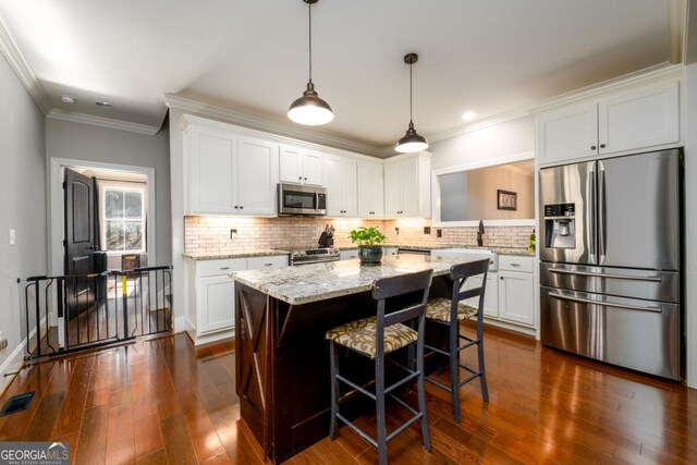 kitchen featuring white cabinetry, stainless steel appliances, a center island, a kitchen bar, and decorative light fixtures