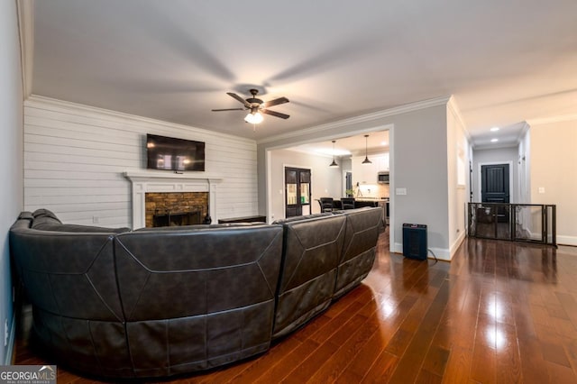 living room featuring hardwood / wood-style flooring, ceiling fan, ornamental molding, and a stone fireplace