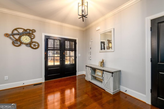 foyer with dark wood-type flooring, ornamental molding, an inviting chandelier, and french doors