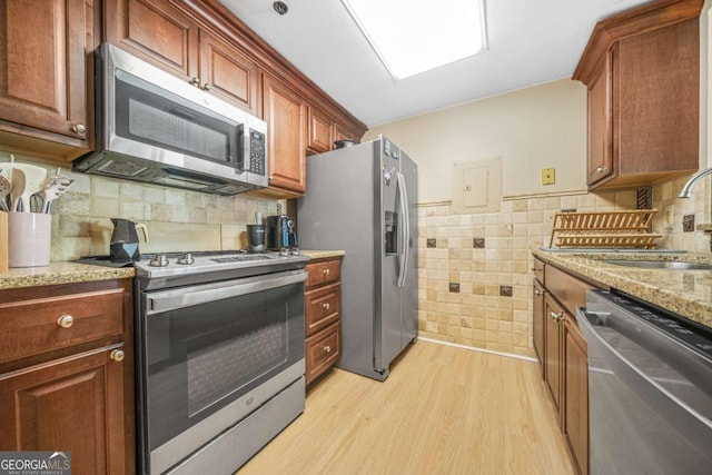 kitchen featuring light wood-type flooring, appliances with stainless steel finishes, sink, and light stone counters