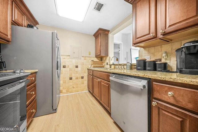 kitchen featuring stainless steel appliances, sink, tile walls, light wood-type flooring, and light stone counters