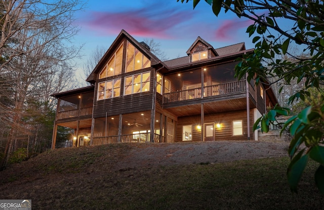 rear view of property featuring a balcony, a sunroom, a garage, and gravel driveway