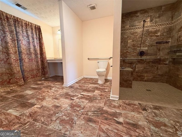 bathroom with a textured ceiling, toilet, and tiled shower