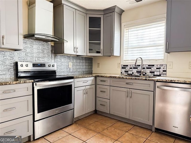 kitchen with light tile patterned floors, stainless steel appliances, wall chimney exhaust hood, and gray cabinets