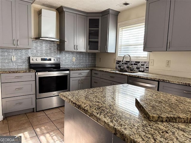 kitchen featuring gray cabinets, appliances with stainless steel finishes, dark stone countertops, wall chimney range hood, and sink