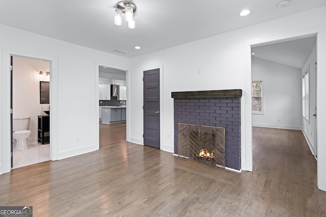 unfurnished living room featuring lofted ceiling, dark hardwood / wood-style floors, and a brick fireplace