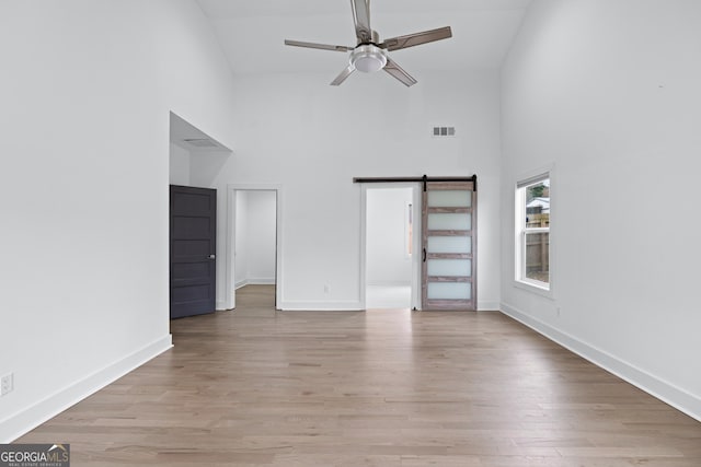 unfurnished living room with ceiling fan, a barn door, high vaulted ceiling, and light hardwood / wood-style floors