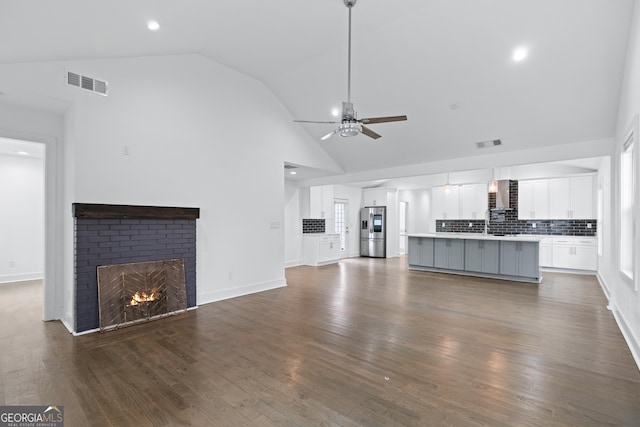 unfurnished living room featuring ceiling fan, dark hardwood / wood-style flooring, high vaulted ceiling, and a fireplace