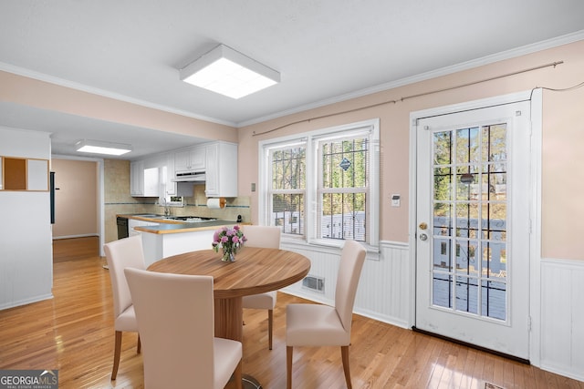 dining space with ornamental molding, sink, and light wood-type flooring