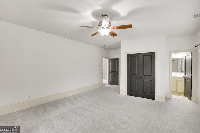 unfurnished bedroom with a closet, ceiling fan, light carpet, and ensuite bath