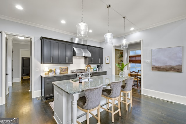 kitchen with an island with sink, sink, a kitchen breakfast bar, hanging light fixtures, and wall chimney exhaust hood