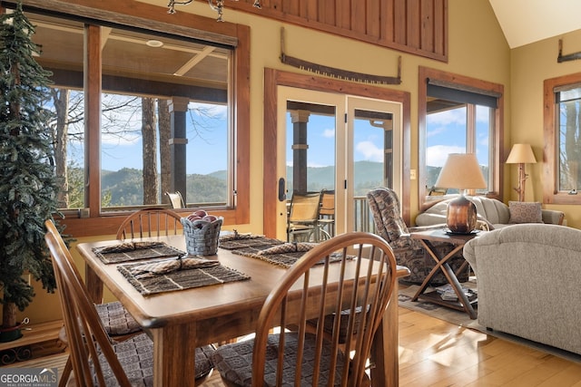 dining room with a mountain view, vaulted ceiling, and light hardwood / wood-style floors