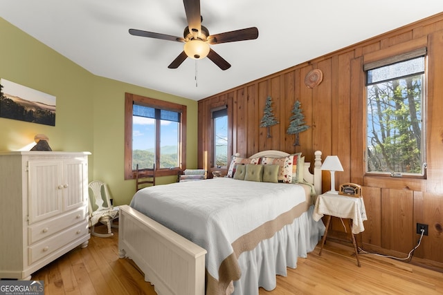 bedroom with ceiling fan, light hardwood / wood-style floors, multiple windows, and wood walls