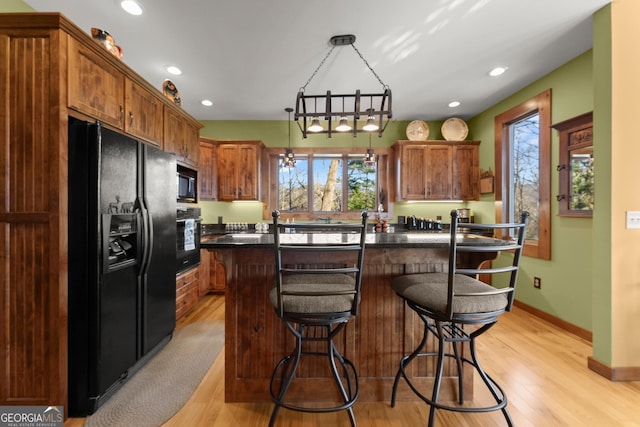 kitchen featuring black appliances, hanging light fixtures, light wood-type flooring, a kitchen island, and a breakfast bar