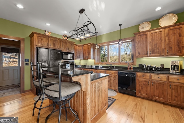 kitchen with black appliances, a center island, sink, decorative light fixtures, and a breakfast bar area