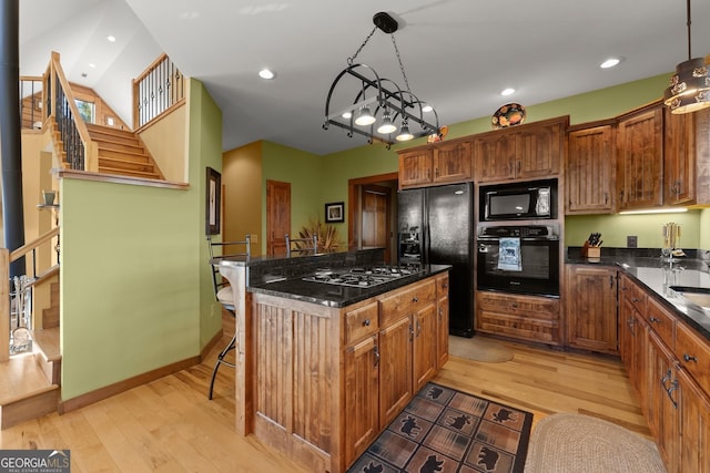 kitchen with black appliances, decorative light fixtures, a center island, and light hardwood / wood-style floors