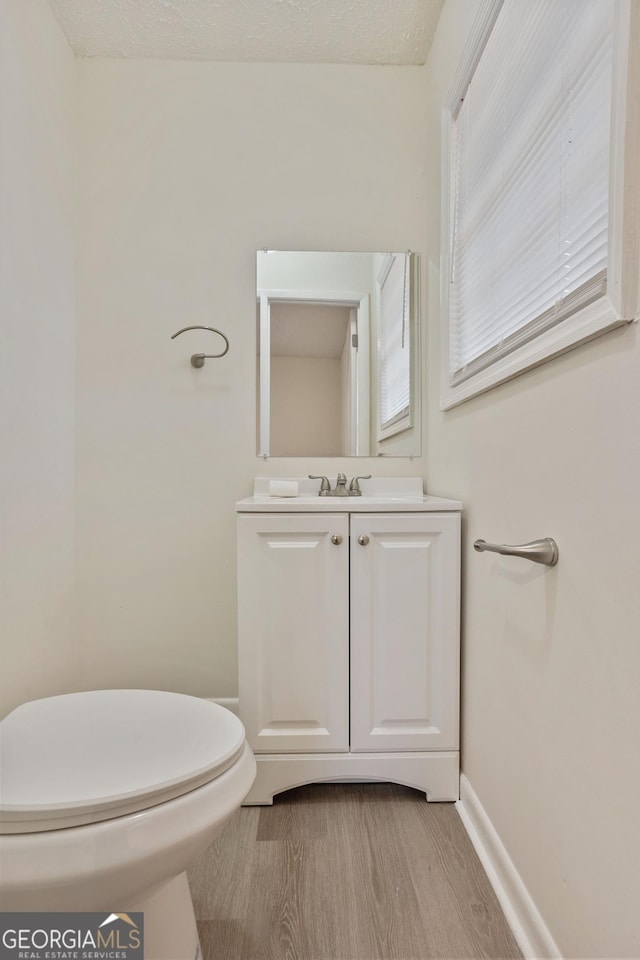 bathroom featuring wood-type flooring, toilet, vanity, and a textured ceiling