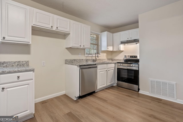 kitchen with sink, white cabinets, light wood-type flooring, light stone counters, and stainless steel appliances