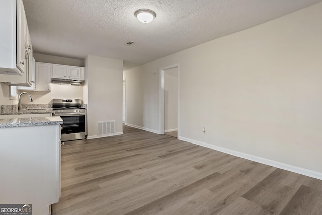 kitchen featuring a textured ceiling, white cabinets, stainless steel range oven, sink, and light stone counters