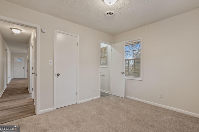 unfurnished bedroom featuring a textured ceiling, light colored carpet, and a closet