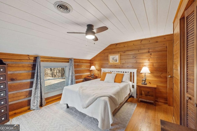 bedroom with vaulted ceiling, wood ceiling, light wood-type flooring, ceiling fan, and wood walls