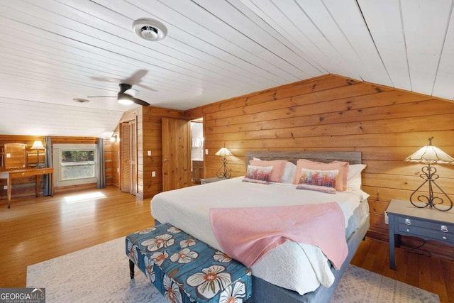 bedroom featuring lofted ceiling, wood ceiling, wooden walls, light wood-type flooring, and ceiling fan