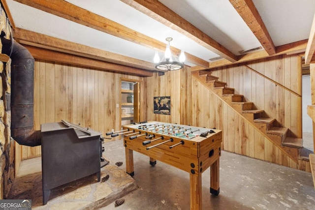 rec room with wood walls, concrete flooring, a wood stove, and beam ceiling