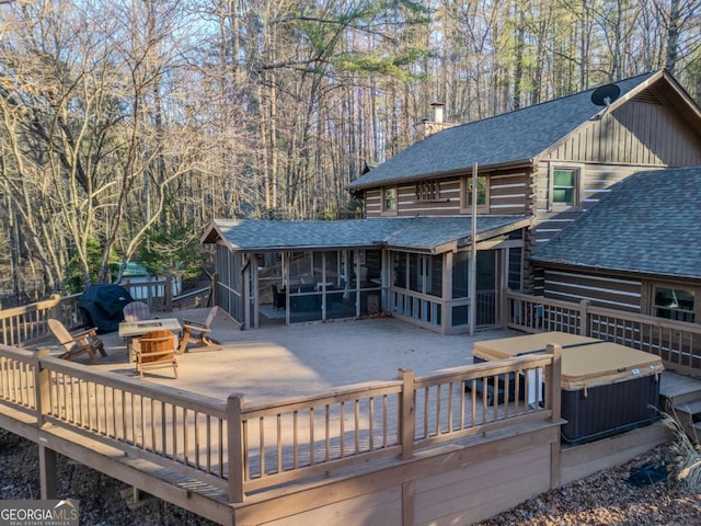 back of property with a fire pit, a sunroom, a wooden deck, and a hot tub