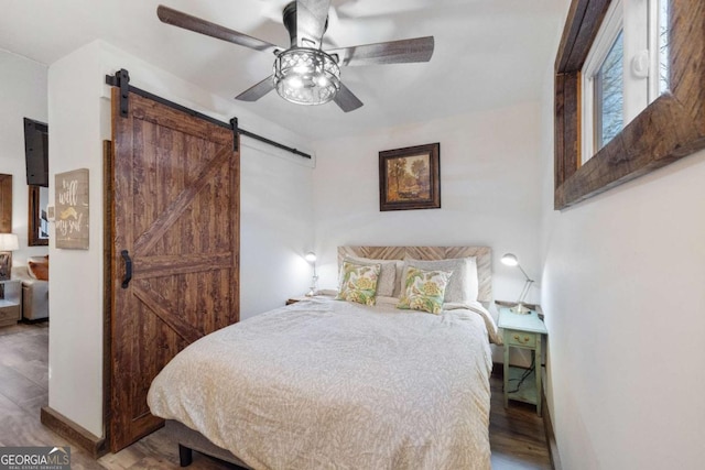 bedroom featuring ceiling fan, wood-type flooring, and a barn door