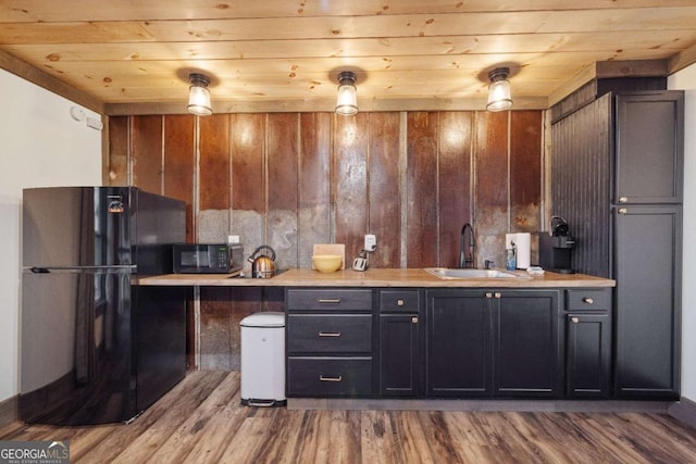 kitchen featuring light hardwood / wood-style flooring, sink, wood ceiling, black appliances, and wooden walls