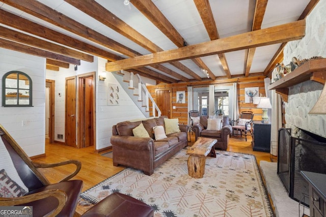 living room featuring light wood-type flooring, beam ceiling, wooden walls, and a fireplace