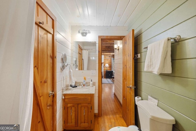 bathroom with hardwood / wood-style flooring, wooden ceiling, toilet, vanity, and wooden walls