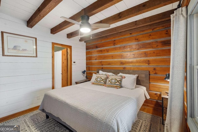 bedroom featuring ceiling fan, beam ceiling, and wooden walls