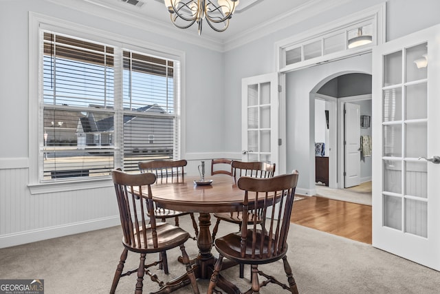 carpeted dining room with crown molding, an inviting chandelier, and french doors