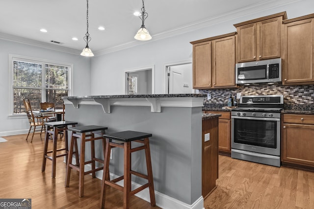 kitchen with pendant lighting, appliances with stainless steel finishes, ornamental molding, and a kitchen island