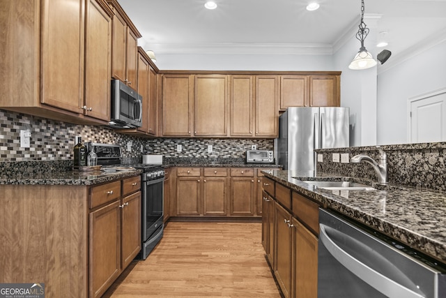 kitchen with crown molding, appliances with stainless steel finishes, hanging light fixtures, sink, and dark stone countertops