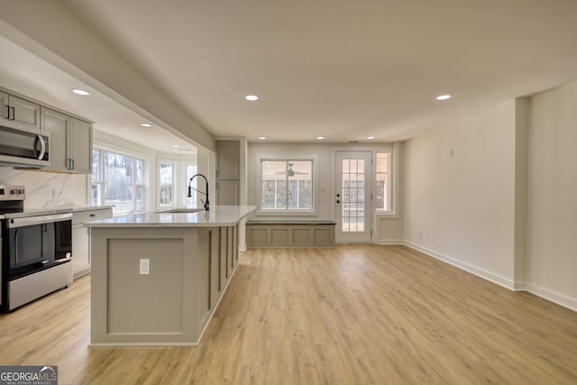 kitchen with a sink, gray cabinetry, light wood-style flooring, appliances with stainless steel finishes, and a kitchen island with sink