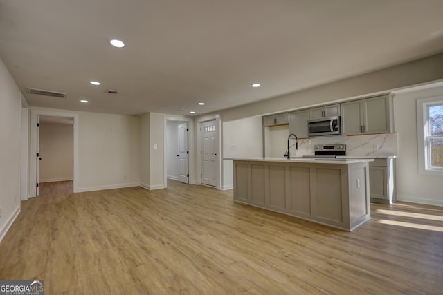 kitchen featuring a kitchen island with sink, gray cabinetry, light wood-type flooring, and stainless steel appliances