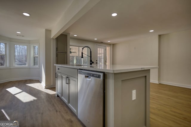 kitchen featuring dishwasher, wood finished floors, a kitchen island with sink, and a sink