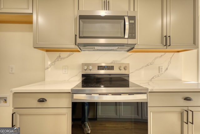 kitchen with decorative backsplash, light stone countertops, dark wood-style flooring, and stainless steel appliances