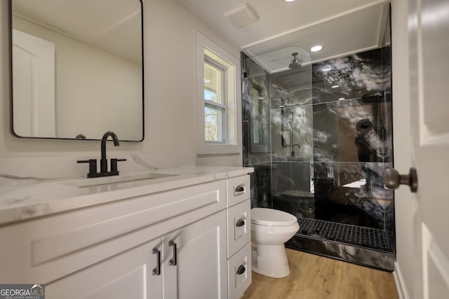 bathroom with a marble finish shower, visible vents, toilet, wood finished floors, and vanity