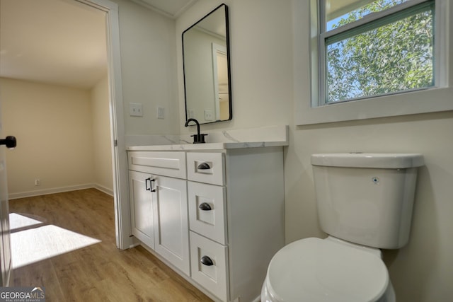 half bath with toilet, vanity, baseboards, and wood finished floors