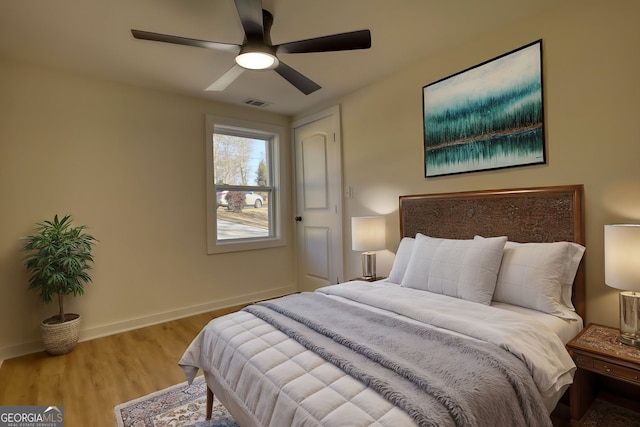 bedroom featuring ceiling fan, visible vents, baseboards, and wood finished floors