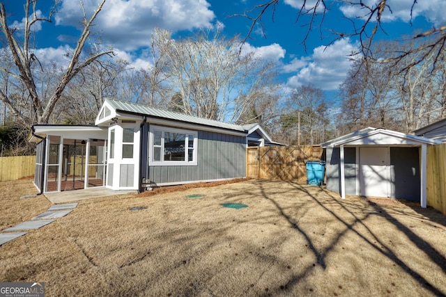 view of property exterior featuring fence, a sunroom, an outdoor structure, a lawn, and metal roof